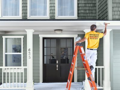 Painter on a ladder painting white trim on a residential house porch