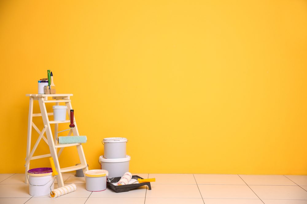 Freshly painted yellow interior wall with ladder and paint tins